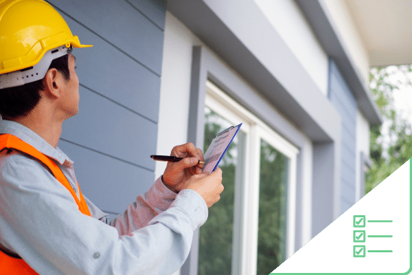 Construction worker holding notepad taking notes looking around exterior of house