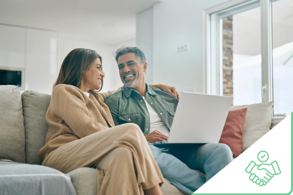 Couple sitting couch smiling at each other with laptop