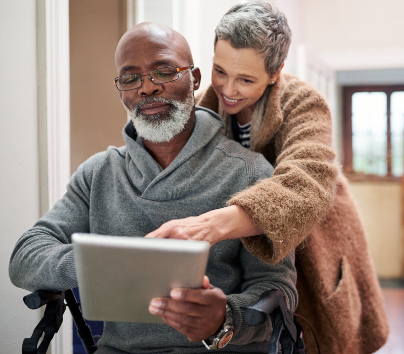 Older diverse couple man in wheelchair looking at tablet in home