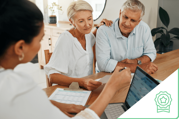 Older couple sitting at kitchen table looking at documents with sales woman