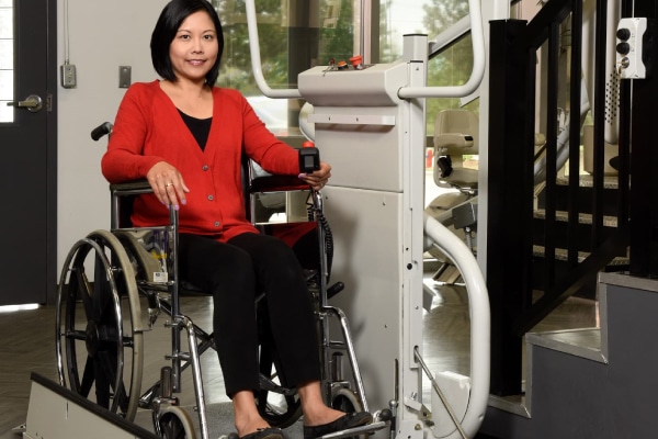 Diverse woman in wheel chair using mobility lift in home to go up stairwell